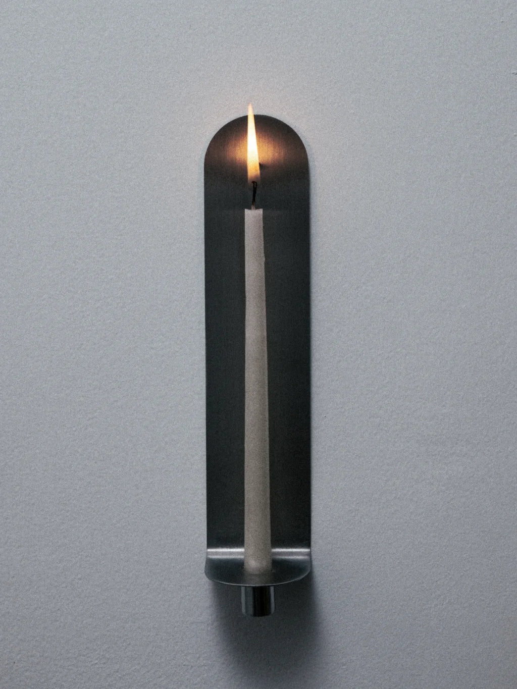 Lámina plegada que se proyecta desde el muro para sostener una vela. Proyecta y refleja la luz.