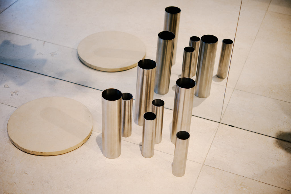 Florero grande. Tiene una tapa perforada que permite sostenerlas en su interior. Fabricado a partir de tubo industrial de acero inoxidable.