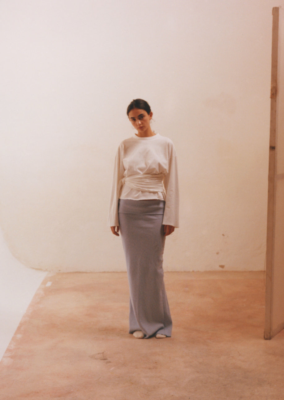 Básico redefinido en algodón con cuello amplio, mangas largas y drapeado lateral que aporta textura y realza la silueta.
Composición: 100% algodón.